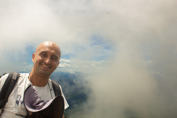 Adult person wearing a t-shirt, comfortable clothes, high in the clouds and with a smile, seeing...