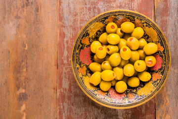 Fresh green olives are presented in an ornate bowl on weathered wooden surface.