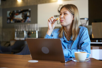 young woman working on laptop computer, eating cookies and drinking a coffee in the cafe