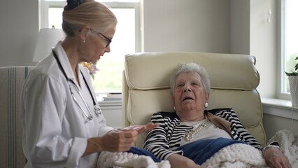 A caregiver attentively speaks with an elderly woman seated in a cozy armchair at home, providing comfort and support during a visit.