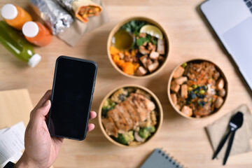 Business people eating healthy meal while working, Businesswoman having a lunch break at the office, hand holding phone with blank black screen for copyspace