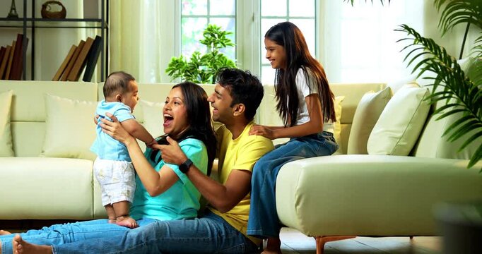 Indian parents and kids smiling while sitting together near sofa on floor in cozy modern living room, looking at camera indoors, enjoying bonding time, family connection, joy, and love at home