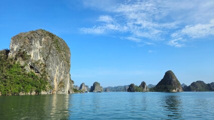 Naklejka premium Towering limestone cliffs frame a serene channel of emerald water in Ha Long Bay, Vietnam, beneath a sky streaked with soft clouds.