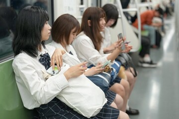 On a spring morning in the Shanghai subway, a group of Japanese high school girls in school uniforms sit on train seats, each quietly lost in her own thoughts during a calm commute in a foreign city.