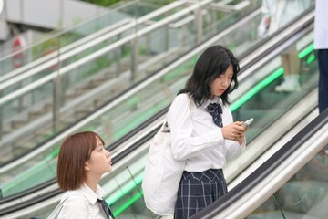 Fototapeta premium In early summer in Shanghai, near The Bund, Japanese high school girls in uniforms ride an escalator, their matching uniforms and quiet chatter adding youthful energy to the vibrant urban atmosphere.