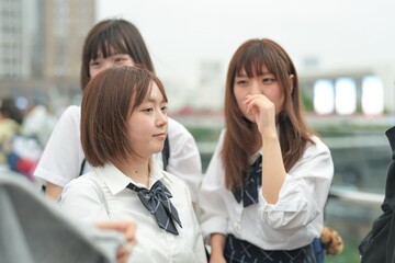 Obraz premium In early summer in Shanghai, near The Bund, Japanese high school girls in uniforms chat and laugh in a busy tourist area, their cheerful presence adding youthful charm to the city's historic vibe.