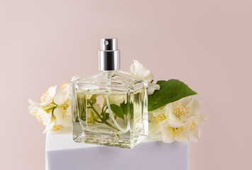 A transparent bottle of women's perfume among jasmine flowers stands on a white podium. Beige...