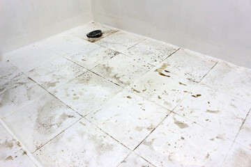 Grime and muddy dirt patches on the floor tiles of a shower room
