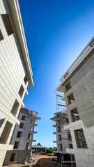 Fototapeta premium Two Modern Residential Buildings Under Final Construction Stage With Scaffolding And Clear Blue Sky, Vertical Composition, Urban Development Concept For Real Estate Marketing And Investment Promotion
