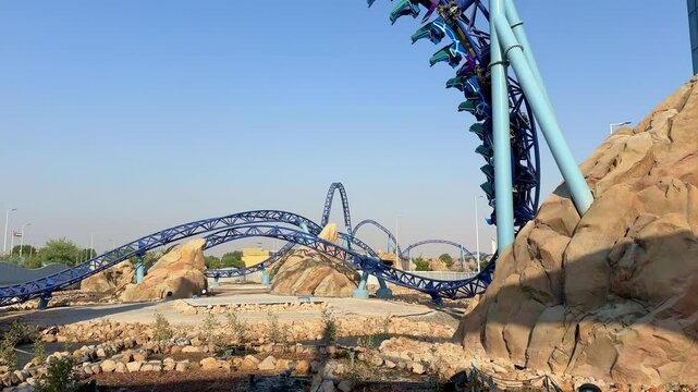 Bright blue roller coaster rushes through loops and curves in a desert-themed amusement park. Thrilling ride, steep turns, and adrenaline-filled fun in a scenic outdoor setting