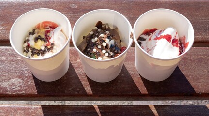 Close-up of frozen Greek yogurt with different toppings in cups outdoors