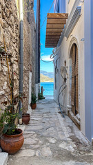 Old Narrow Alley With Stone Walls And Potted Plants Facing The Sea In A Mediterranean Village, Captured In Summer, Concept Of Travel, Escape, Vacation