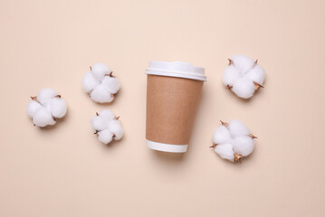 Disposable cardboard coffee cup and cotton flowers on beige background