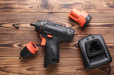 Modern cordless screwdriver with charger on wooden table. Top view