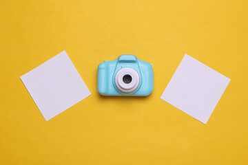Toy plastic camera with blank cards on yellow background