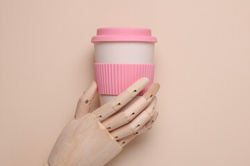 Wooden puppet hand holding eco plastic coffee cup on beige background