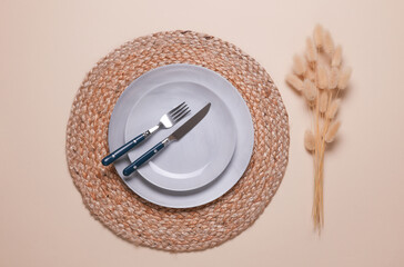 Example of aesthetic table setting. Straw woven rug with plate and cutlery on beige background