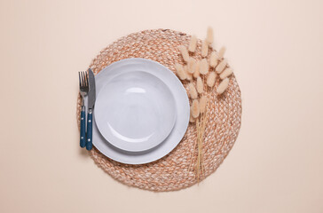 Example of aesthetic table setting. Straw woven rug with plate and cutlery on beige background