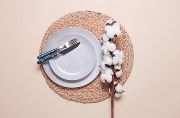 Example of aesthetic table setting. Straw woven rug with plate and cutlery on beige background