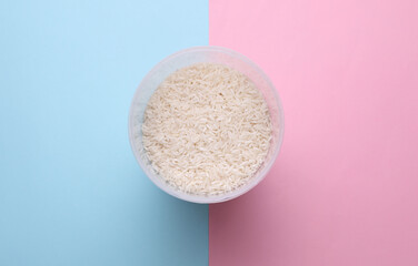 Plastic jar with rice on blue pink background. Top view