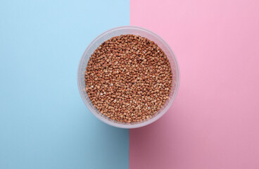 Plastic jar with buckwheat on blue pink background. Top view