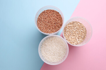 Plastic jars with buckwheat, oatmea and rice on blue pink background. Top view