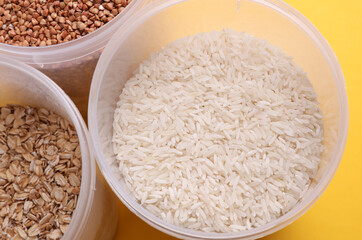 Plastic jars with buckwheat, oatmea and rice on yellow background. Top view