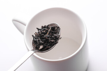 Green tea leaves in spoon on cup background.
