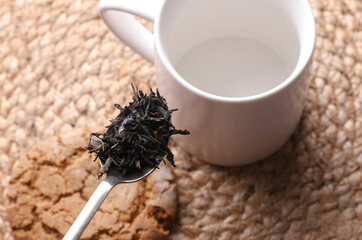 Black tea leaves in spoon on cup background.