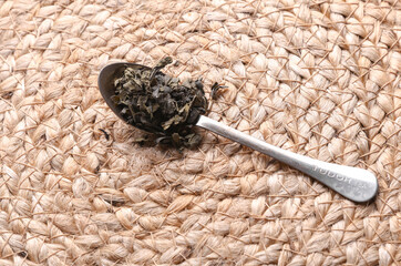 Green tea leaves in a spoon on a straw mat background