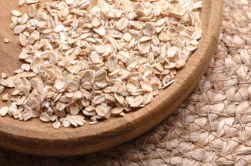 Oatmeal flakes in a wooden bowl on a straw mat