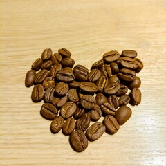A warm and inviting image featuring freshly roasted coffee beans meticulously arranged into a heart shape on a clean wooden surface