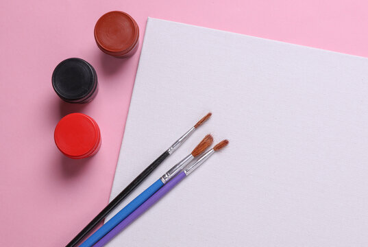 Set for drawing, children's creativity. White blank canvas, paint jars and brushes on pink background. Top view. Flat lay