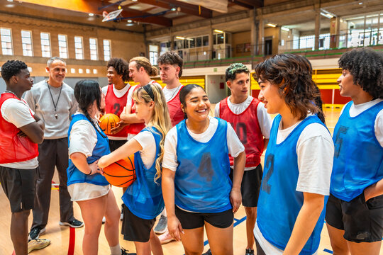 Diverse high school basketball team listening to coach's instructions in gym