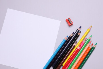White blank paper sheet and Set of wooden colored pencils with sharpener on gray background