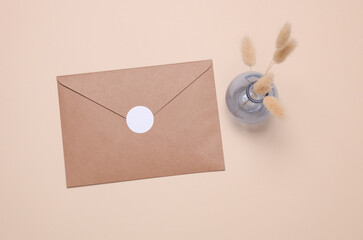 Kraft envelope with white sticker and vase with dried flowers on beige background. Top view