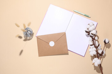 Open notebook or diary and envelope, cotton flower on beige background. Top view