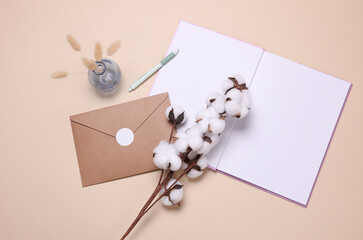 Open notebook or diary and envelope, cotton flower on beige background. Top view