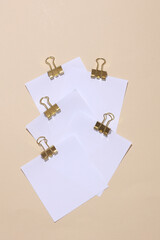 White blank square memo paper cards with gold binder clips on beige background. Mockup for design