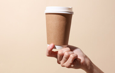 Craft cardboard coffee cup in female hand on beige background