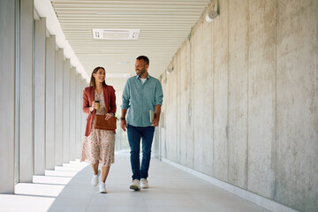 Full length of happy colleagues walking though hallway of office building.