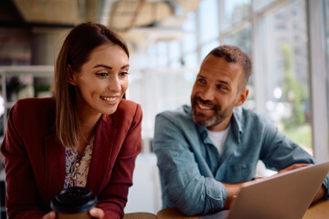 Happy businesswoman and her colleague using laptop while working in office.