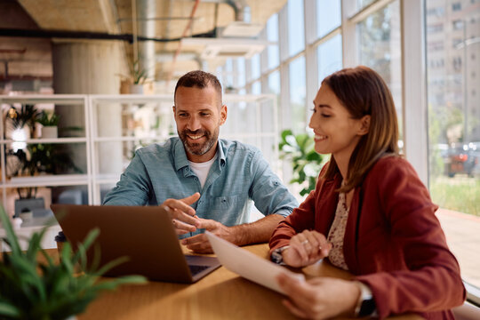 Happy colleagues cooperating while working on laptop in office.