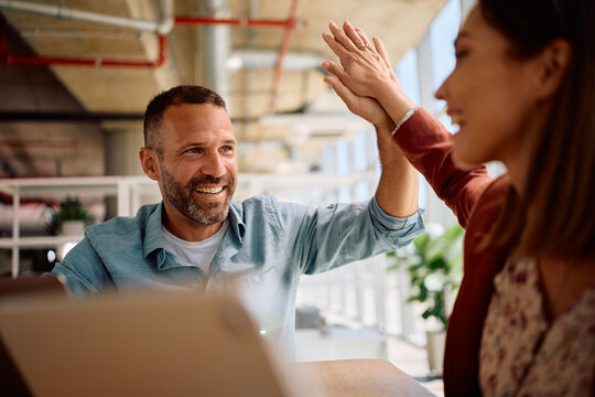 Happy entrepreneur giving high-five to his colleague while celebrating their business success in office.