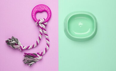 Dog rubber toy with rope and food bowl on pastel background