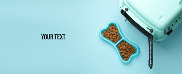Pet carrier box and bowl of dry food on blue background. Top view. Copy space for your text
