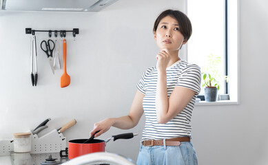 キッチンで料理をしながら悩んでいる女性