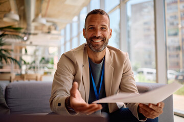 Happy businessman analyzing reports during video call in office and looking at camera.