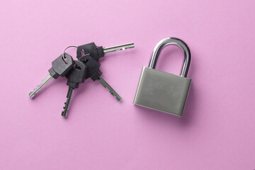 Closed metal lock with keys on a pink background