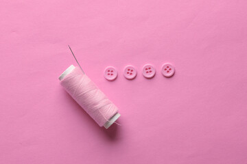 Skein of pink thread and needle, buttons on pink background. Sewing accessories